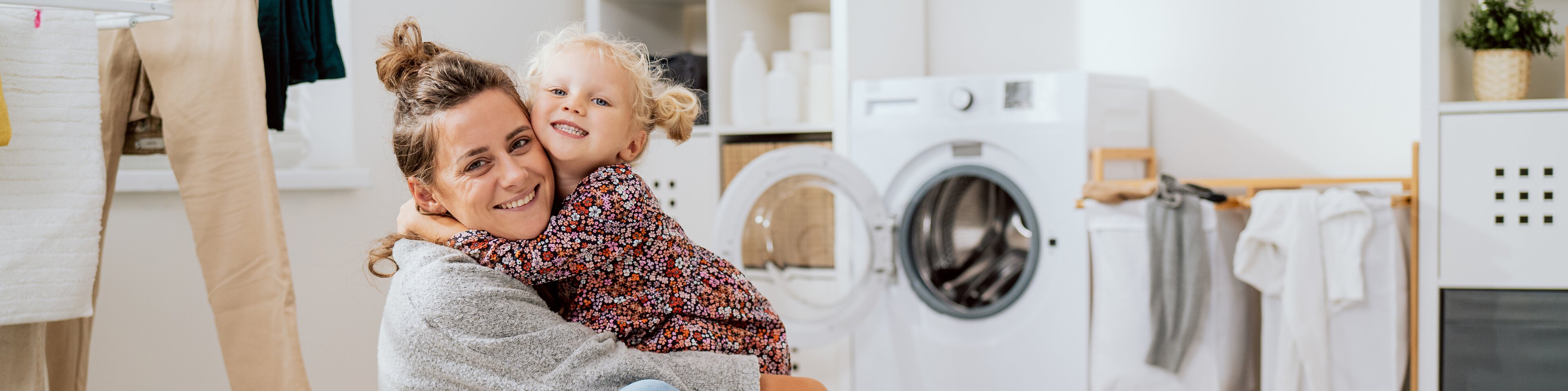 Eine Frau sitzt mir ihrem Kind auf dem Boden neben einem vollen Wäschekorb und vor einer Waschmaschine | © bpilewski - ABCreative - stock.adobe.com